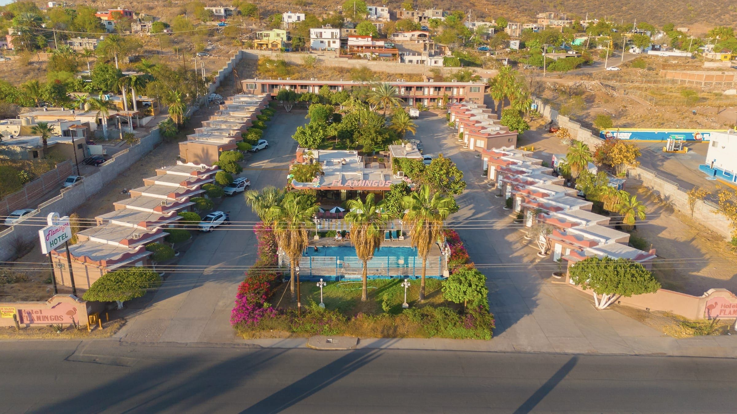 Vista aérea de Hotel Flamingos: jardín central, alberca y habitaciones con los cerros de Guaymas al fondo